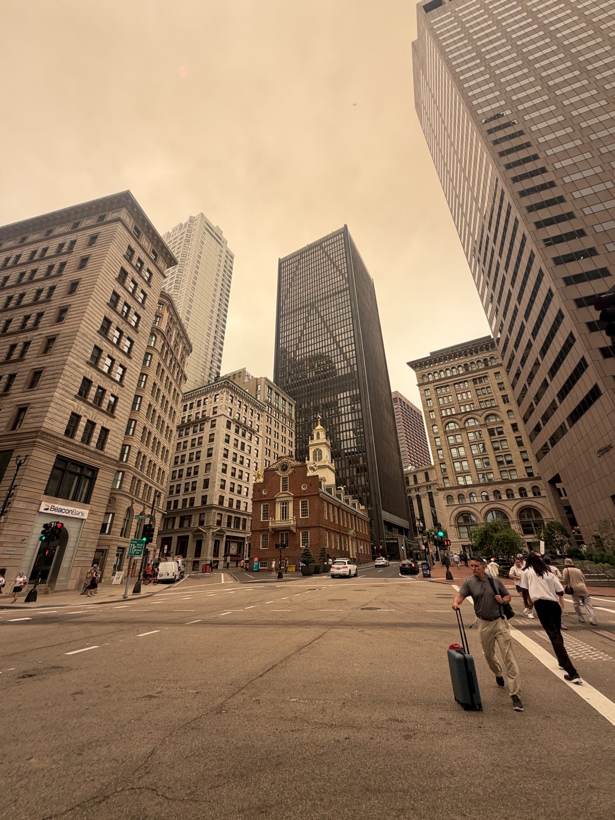 Downtown Boston under a smoke-orange sky, someone crossing the intersection by the Old State House.
